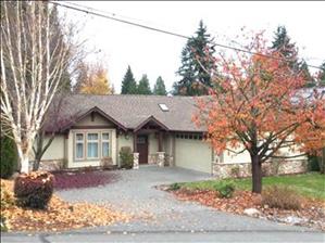A one story house with trees and autumn leaves in front. 